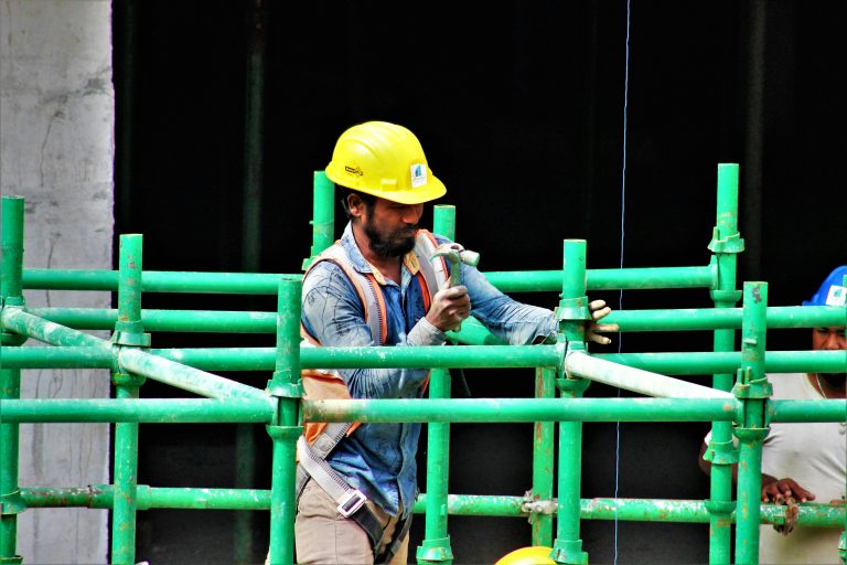 Worker assembling green scaffolding on a construction site